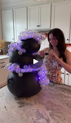 a woman standing in front of a black pot with purple lights on top of it