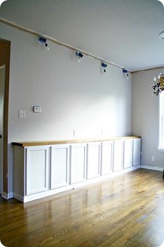 an empty living room with hard wood flooring and white painted cabinets on the wall