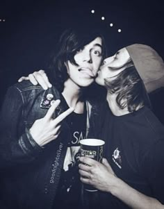 two people kissing each other while holding coffee cups in their hands and posing for the camera