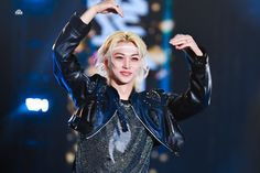 a woman with blonde hair and black leather jacket holding her hands up in the air