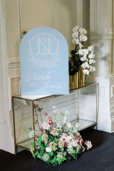 a blue sign sitting on top of a table next to white flowers and greenery