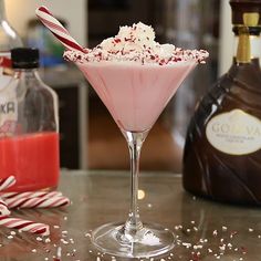 a pink drink with candy canes and sprinkles on the table next to liquor bottles