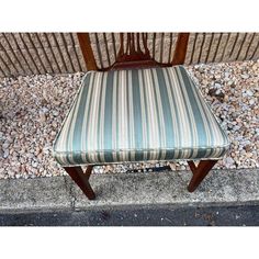 a wooden chair sitting on top of a sidewalk next to a gravel covered ground with rocks