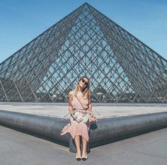 a woman sitting on a ledge in front of the pyramid at the musee d'art