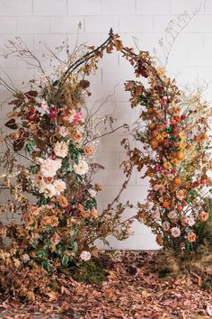 an arch made out of branches and flowers with leaves on the ground next to it