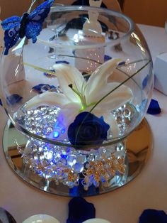 a glass bowl filled with white and blue flowers on top of a table next to candles