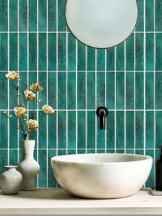 a bathroom sink sitting under a mirror next to a white vase with flowers in it