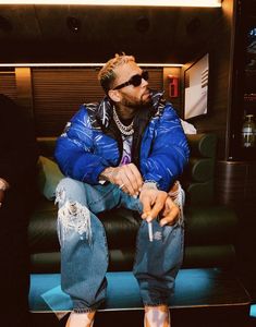 a man sitting on top of a black couch wearing ripped jeans and a blue jacket