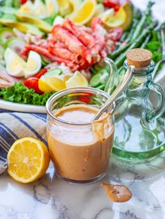 a glass jar filled with dressing next to a plate of salad and lemon wedges