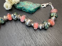 "Perfect for spring and summer, this adjustable bracelet features gorgeous artisan lampwork glass beads that are peach pink on one side and speckled green and blue on the other, combined with pink glass rondelles, green and brown speckled glass rondelles, and accented with gleaming with sterling donuts and Bali granulated sun and daisy spacers, and green and pink Swarovski crystals. Finished with a Silver plated lobster clasp an extension chain with charm. Fits as an approximately 6 7/8 inch bra Handmade Peach Bracelets With Round Beads, Handmade Peach Beaded Bracelets For Gift, Handmade Peach Beaded Bracelets As Gift, Handmade Pink Glass Bracelets, Pink Glass Beaded Bracelets As Gift, Unique Pink Jewelry With Spacer Beads, Adjustable Pink Glass Bracelets, Unique Pink Bracelets As Gift, Unique Pink Bracelets For Gifts