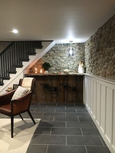 a living room with stone walls and flooring next to a stair case in the corner