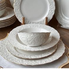 a stack of white dinner plates with gold trimmings on each plate, and an empty bowl in the middle