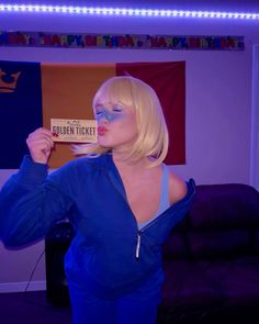 a blonde woman with blue makeup holding up a sign that says golden ticket in front of her face