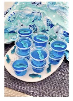 blue jello cups sitting on top of a plate next to an ocean themed cloth