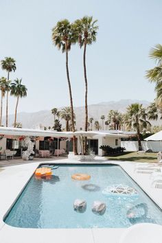 an empty swimming pool surrounded by palm trees and lawn chairs in front of a house