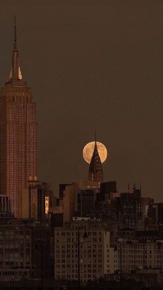 the full moon is seen over new york city's skyscrapers in this image