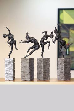 three sculptures of people jumping over stacks of stacked rocks in front of a painting on the wall