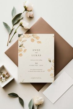 the wedding stationery is laid out on top of an envelope with flowers and greenery