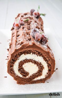 a chocolate roll with icing and cranberries is on a white platter