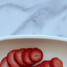 sliced strawberries in a white bowl on a marble table