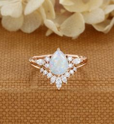 a white opal and diamond ring sitting on top of a table next to flowers