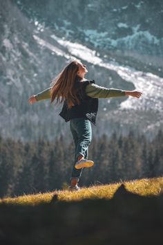 a woman with long hair is jumping in the air on top of a grassy hill