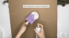 a hand holding a purple and white duster in front of a cardboard box that says use hairdry to secure the glitters