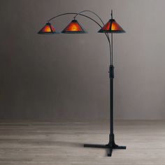 three light floor lamp with orange shades on the lampshade and black stand against a gray wall