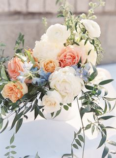 an arrangement of flowers and greenery on top of a white cake with frosting