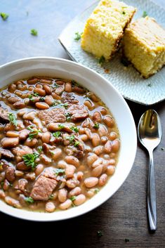 a white bowl filled with beans and meat next to a piece of cake