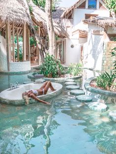 a woman laying in the middle of a pool next to some trees and water features