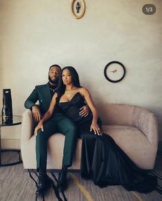 a man and woman sitting on a couch in front of a wall with a clock