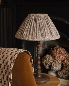 a lamp sitting on top of a wooden table next to a chair and fire place