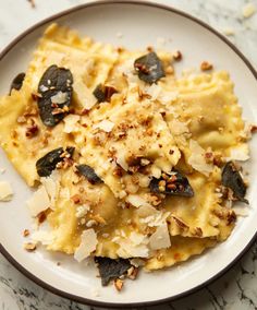 a white plate topped with pasta covered in cheese and toppings on top of a marble table