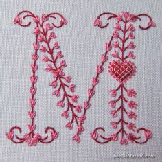 the letter m is made up of pink thread and has a heart on it's side