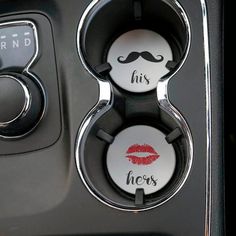 two buttons with the words his and hers written in red lipstick on them, next to a steering wheel knob