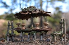 an umbrella made out of wood and moss sitting on top of a table in the woods