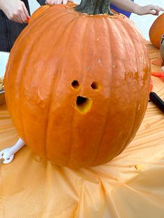 a person carving a pumpkin with scissors and other tools on a yellow tableclothed surface