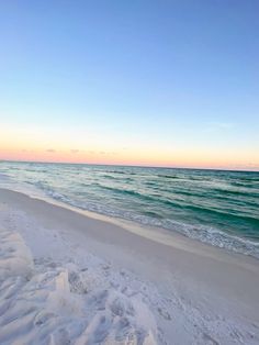 the beach is covered in white sand and blue water as the sun sets over the ocean