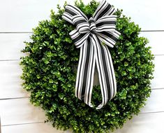 a black and white bow on top of a boxwood wreath