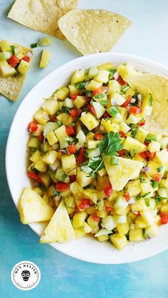 a white bowl filled with pineapple salsa next to tortilla chips and cilantro