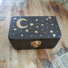 a small wooden box with stars and the moon painted on it's lid sitting on a wood floor