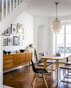 a dining room table with chairs and pictures on the wall above it in front of a staircase