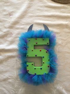 the letter e is decorated with blue and green feathers, and has horns on it