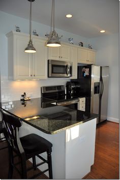 a kitchen with white cabinets and black counter tops, two stools at the island