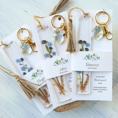 five key chains with flowers and leaves on them are tied to twine, sitting on a white surface