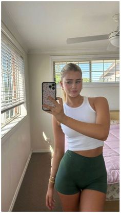 a woman taking a selfie with her cell phone in front of the camera while wearing green shorts