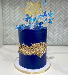 a blue and gold birthday cake with butterflies on top, sitting on a white table