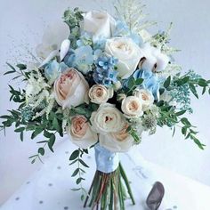 a bridal bouquet with blue and white flowers on a table next to high heel shoes