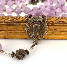 Artisan crafted featuring soft lavender Cape Amethyst gemstones, Swarovski crystals and bronze. Amethyst’s beautiful coloring makes it one of the most prized members of the quartz family. These soft lavender faceted beads provide a gorgeous contrast to the vintage bronze pieces in this heirloom rosary. The elegant center is an antique replica of the profile of Our Lady of Lourdes and measures 1.” This very versatile center pairs nicely with most crucifixes! In this rosary, we have combined it wi Spiritual Amethyst Gemstones With Accents, Amethyst Gemstones With Spiritual Style, Faceted Amethyst Spiritual Gemstone, Spiritual Amethyst Gemstones, Lavender Amethyst Crystals For Gift, Spiritual Lavender Crystals For Gifts, Lavender Spiritual Crystals For Gift, Lavender Amethyst Crystals As A Gift, Collectible Spiritual Purple Necklace